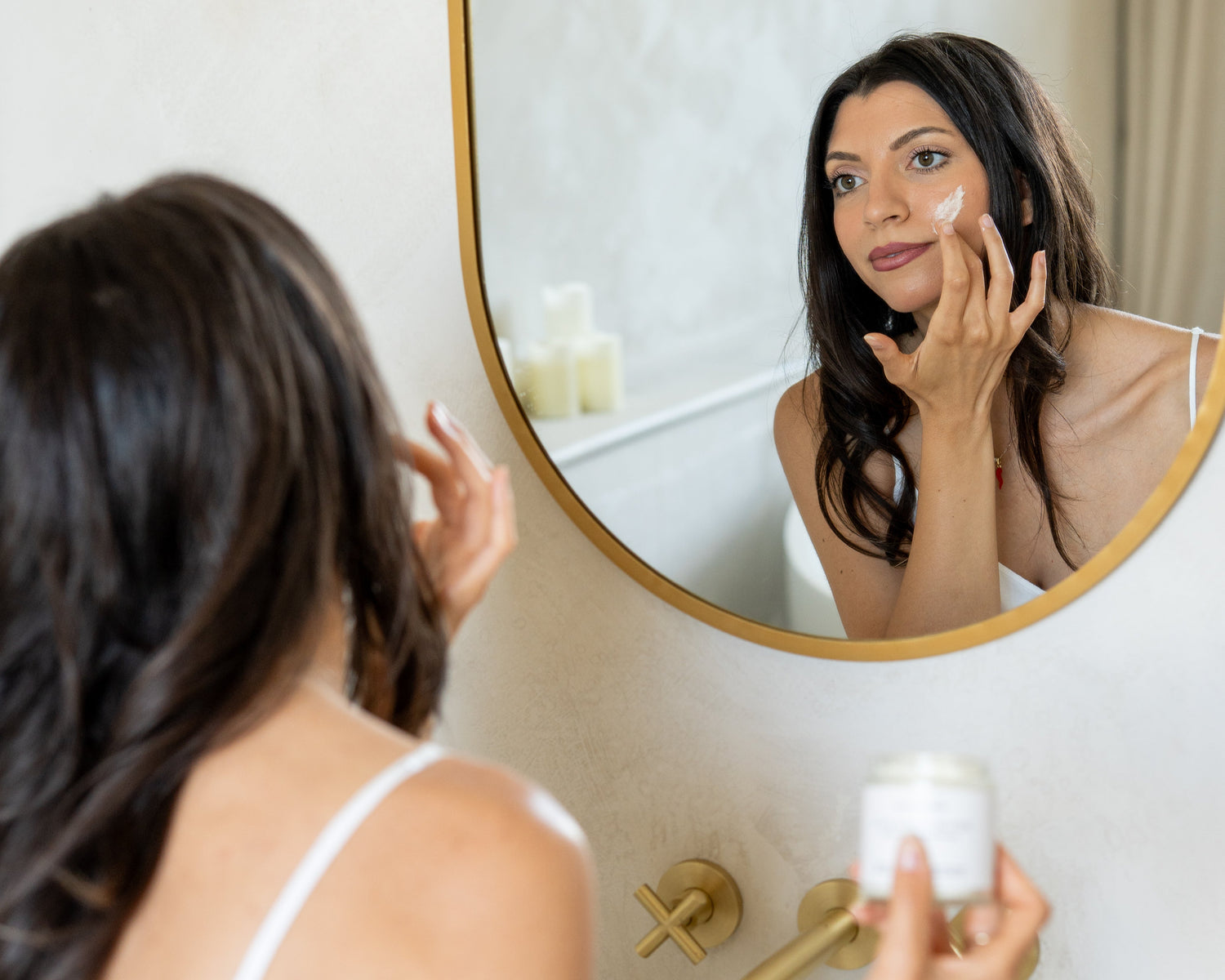 Woman applying cream to her face in front of a mirror